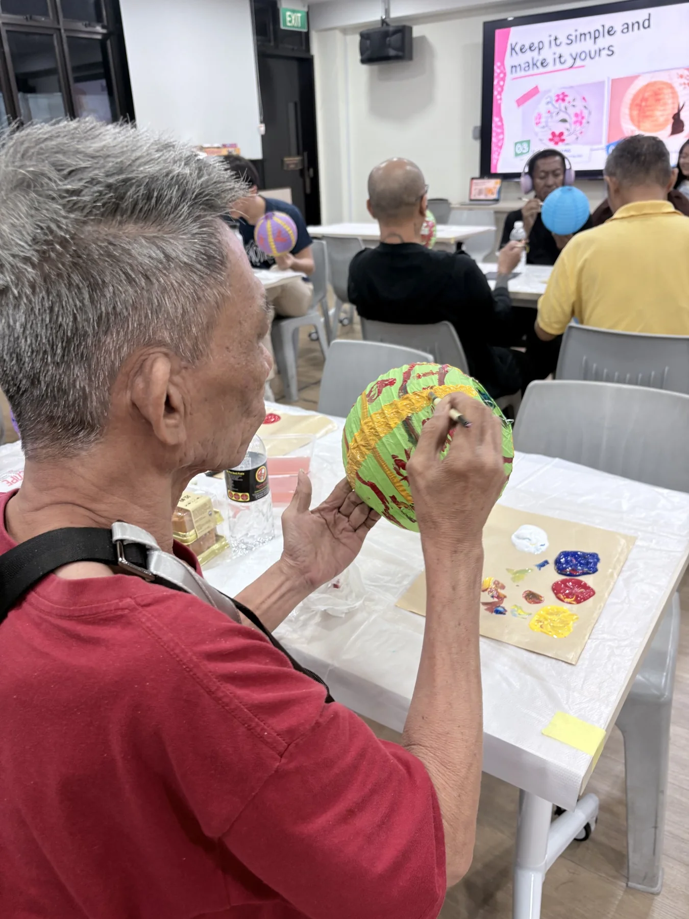 Older participant carefully painting a colourful paper lantern during a community art workshop